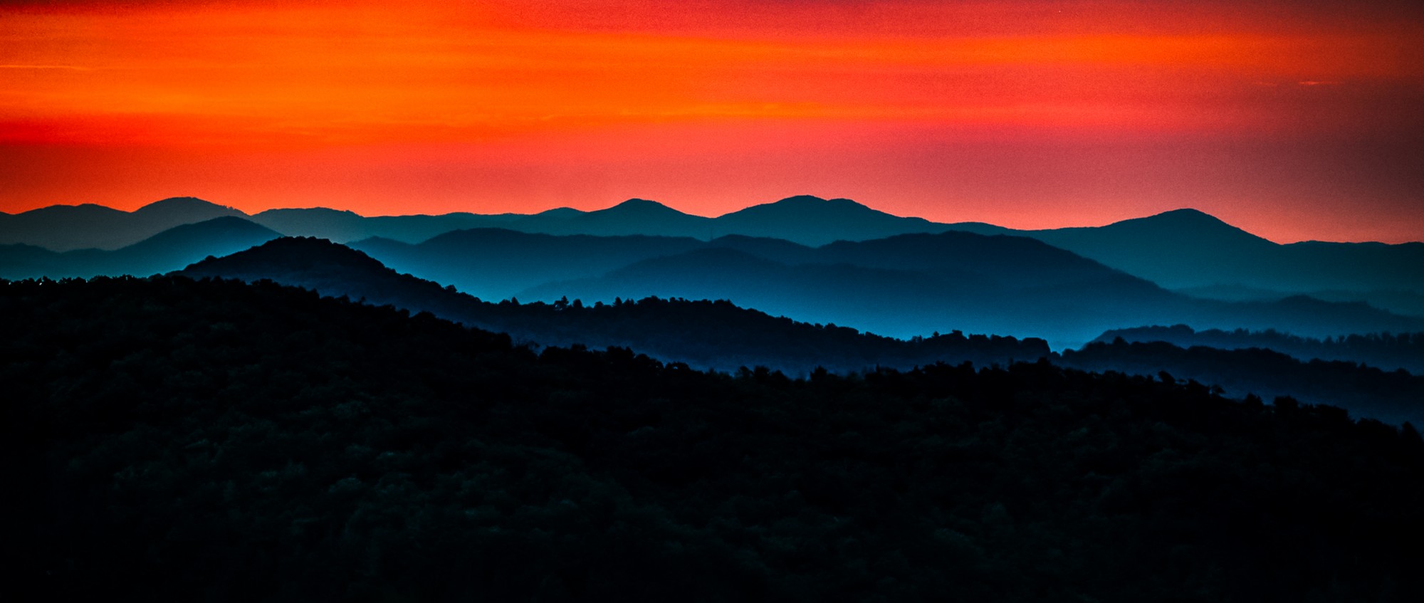 Layered blue mountain ridges beneath a blazing red sky