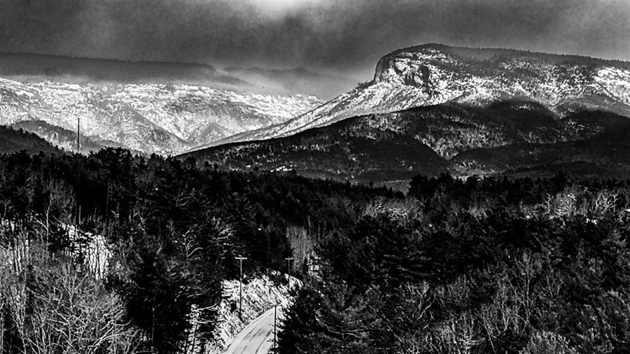 Black and white view of snow-dusted mountains above a winding road
